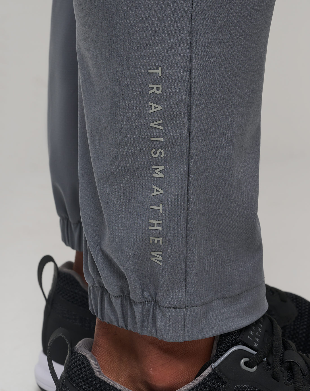 Detail shot of the Open to Close Jogger in grey showing the elastic cuff and TravisMathew logo.