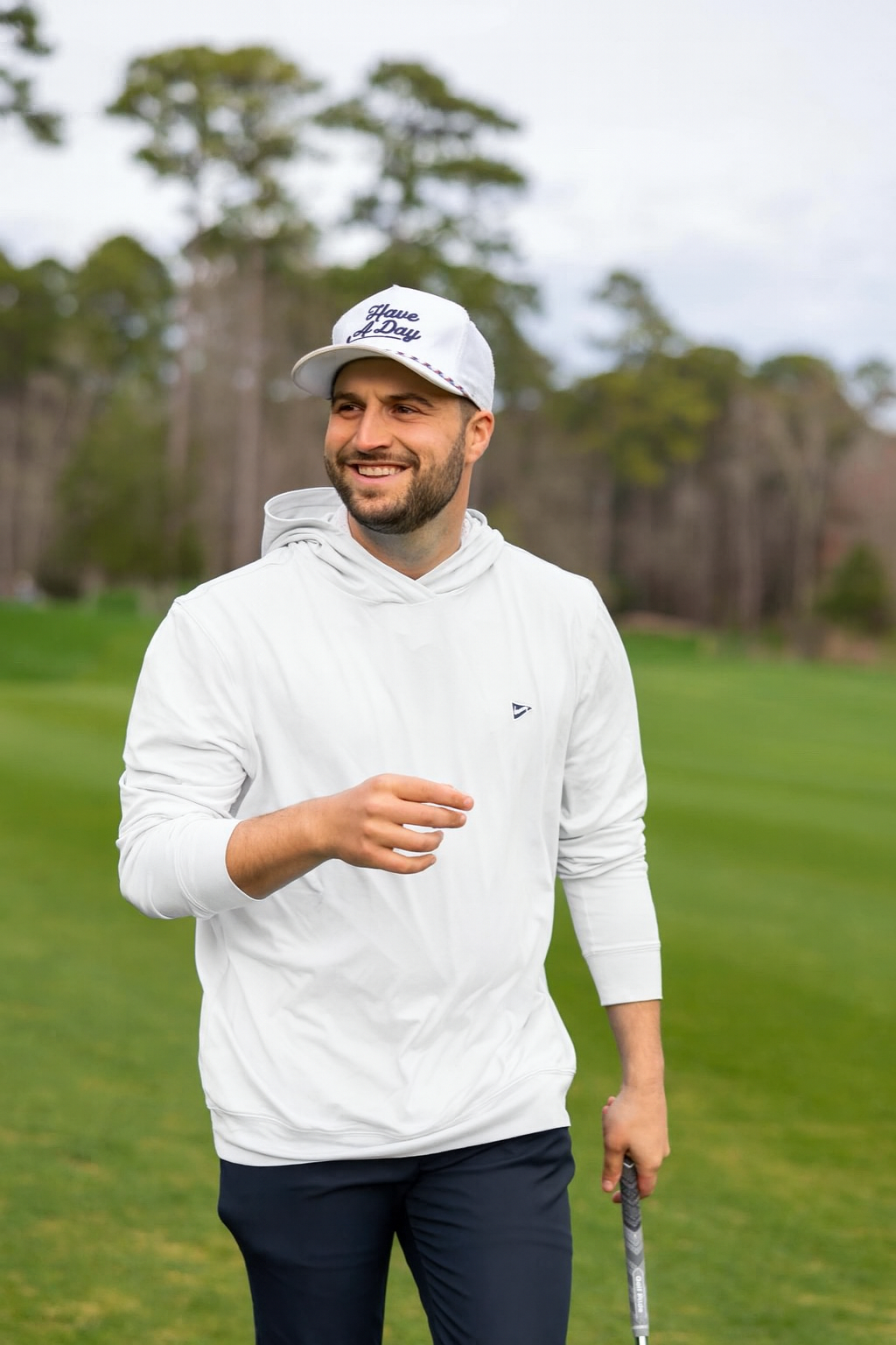 Man wearing a white hoodie and cap on a golf course