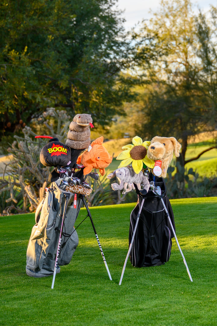 Golf bags on a course featuring Daphne’s novelty animal golf headcovers including yellow lab, snake, fish, flower, and elephant designs.
