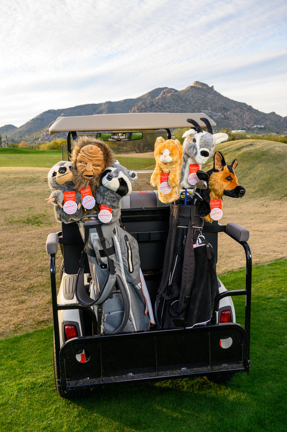 Golf cart carrying golf bags with Daphne’s animal golf headcovers including raccoon, lion, cat, goat, and dog designs on a golf course.