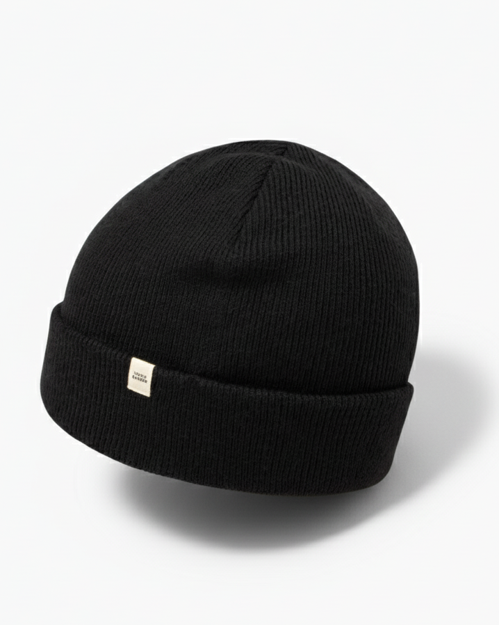 TravisMathew Cloud Beanie in black – minimalist rib-knit winter hat with small woven logo tag, shown on a clean white background.