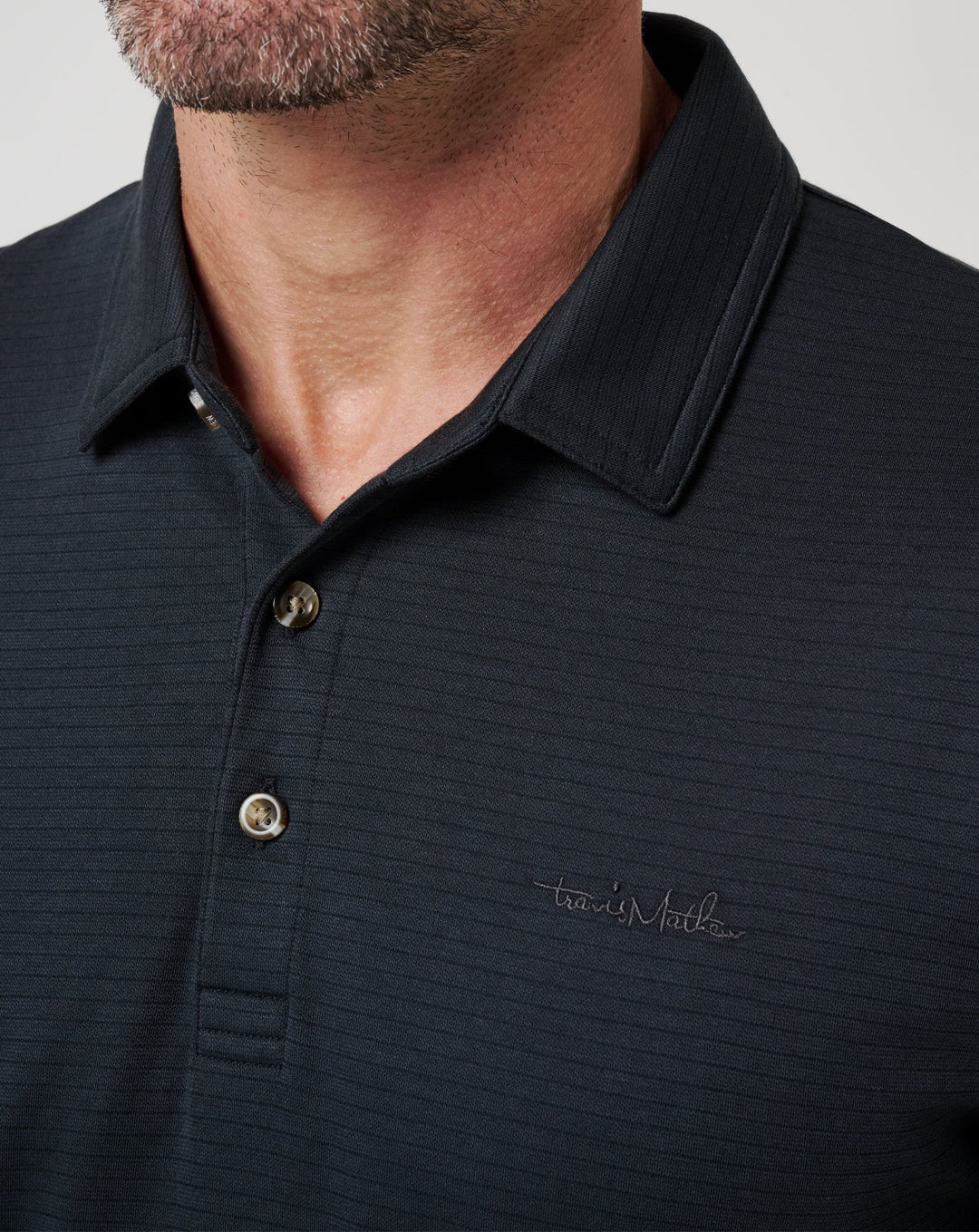 Close-up of Zinna 2.0 polo collar showing textured performance fabric and button placket in black