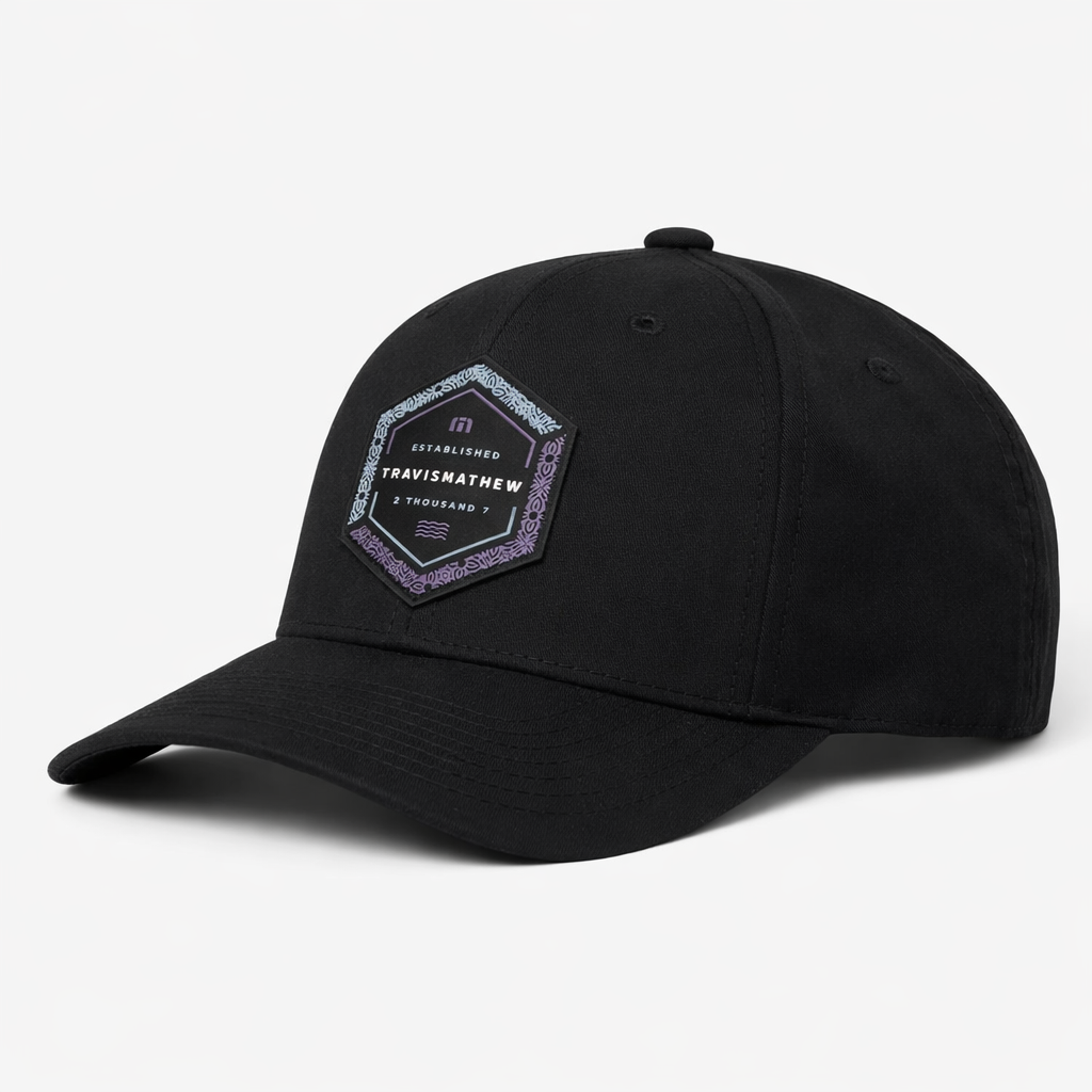 TravisMathew Word of Mouth snapback hat in black with hexagon logo patch, angled front view