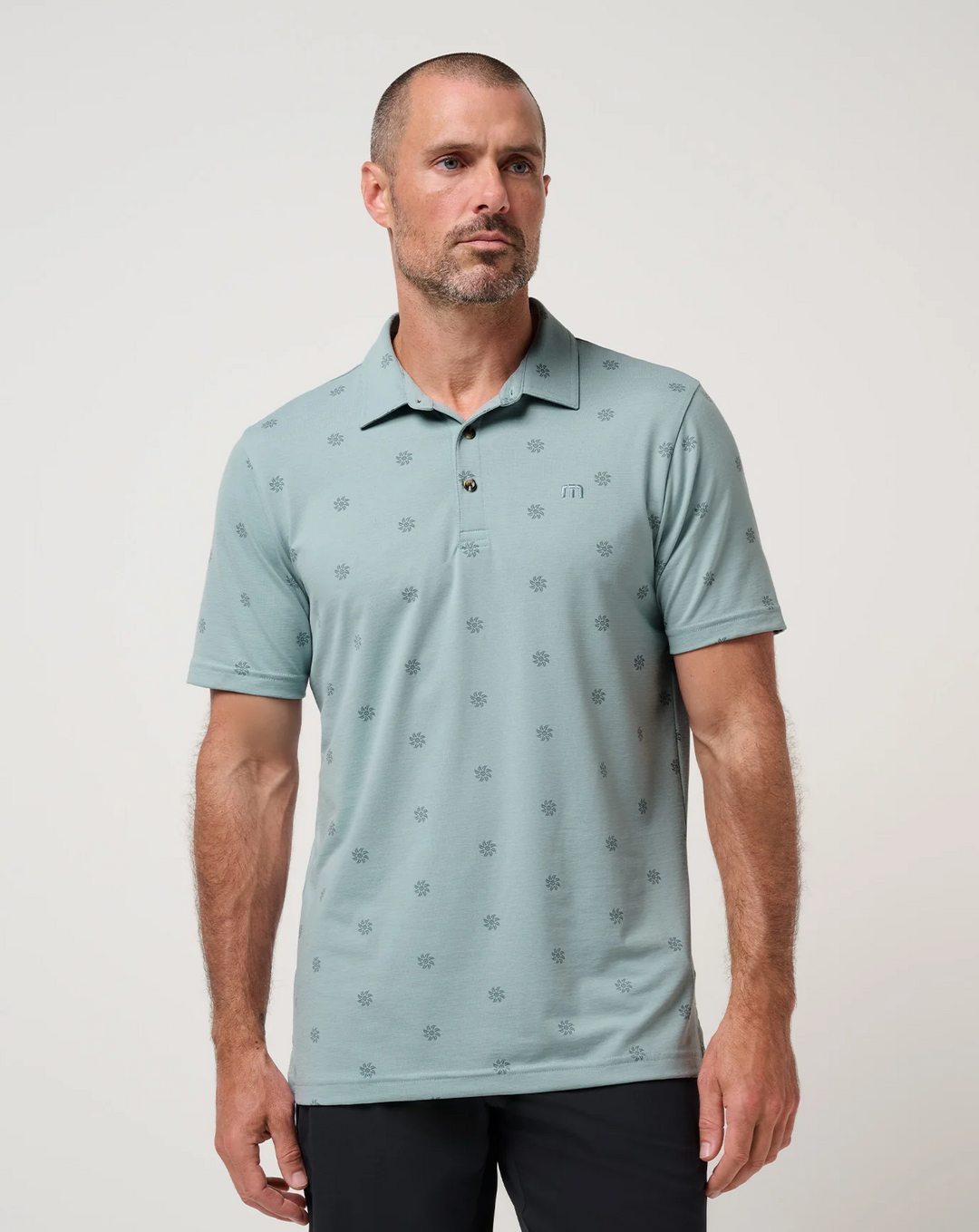 TravisMathew Performance Jersey Sol Polo in muted green with subtle all-over sunburst print, shown from the front on model