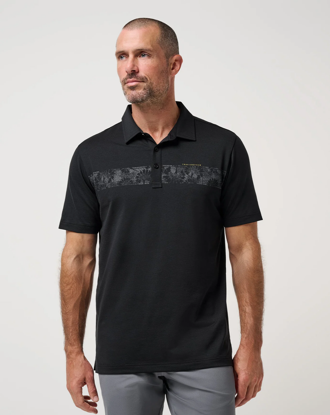 Model wearing the TravisMathew Performance Jersey Flight Polo in black with chest stripe