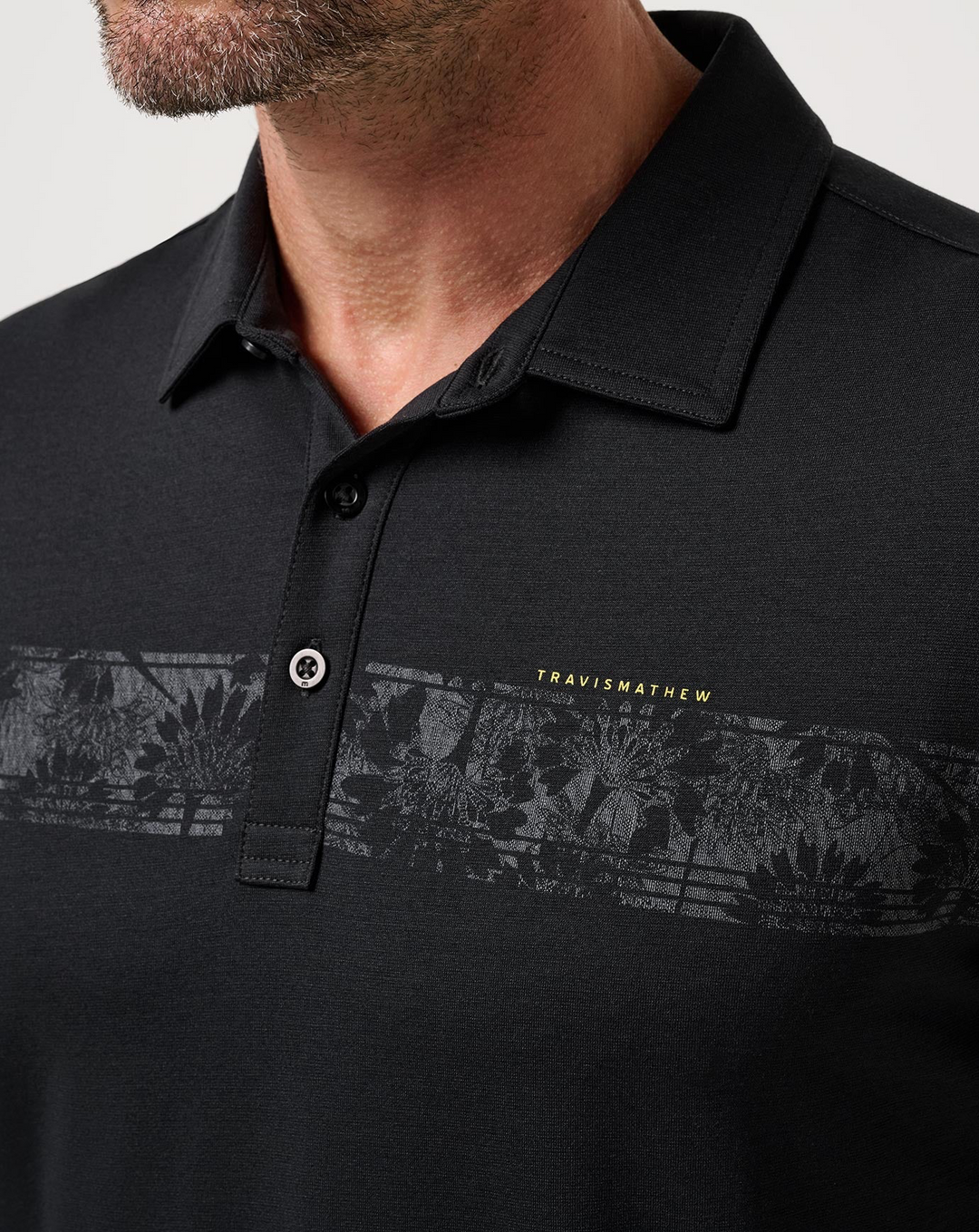 Close-up of the TravisMathew Performance Jersey Flight Polo highlighting the collar, buttons, and tonal floral chest stripe