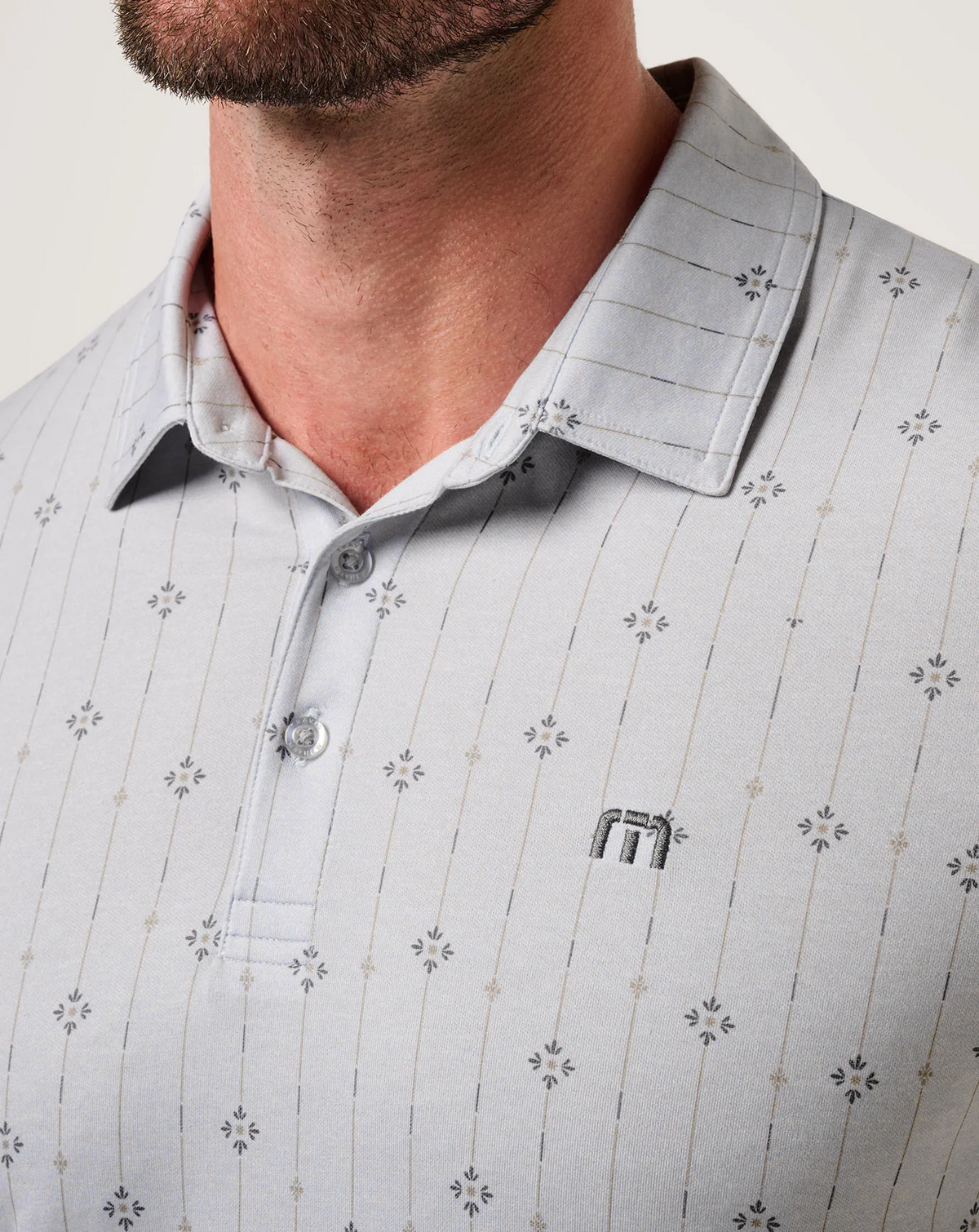 Close-up of the TravisMathew Featherweight Deco Polo collar, button placket, and subtle geometric pattern with embroidered logo