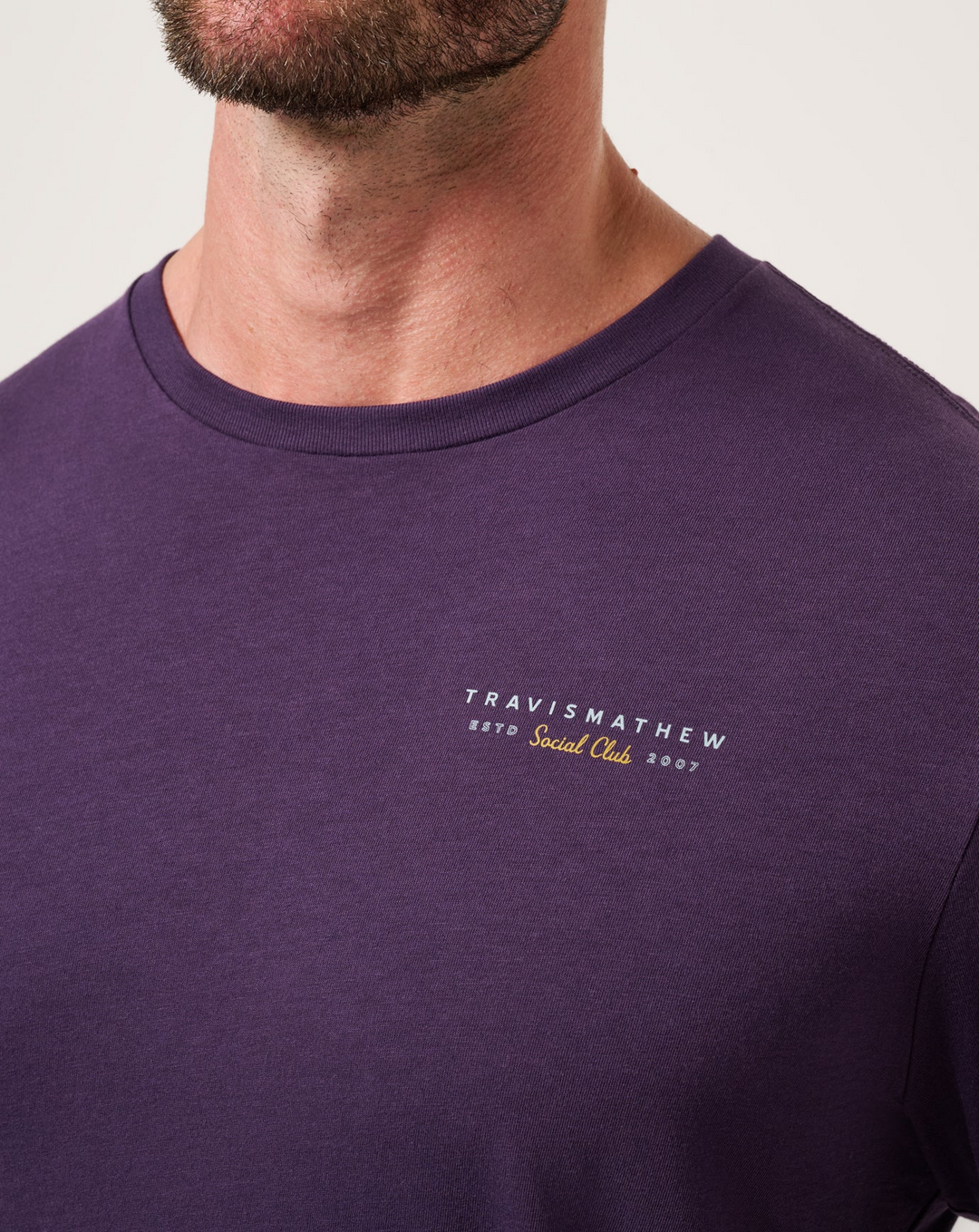 Close-up of TravisMathew Social Hour T-Shirt chest logo in purple