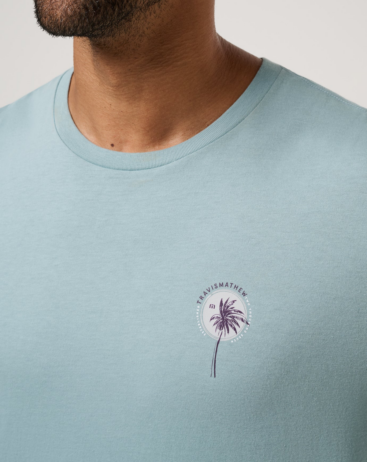 Close-up of palm tree chest graphic on TravisMathew Hold My Calls Tee in light blue