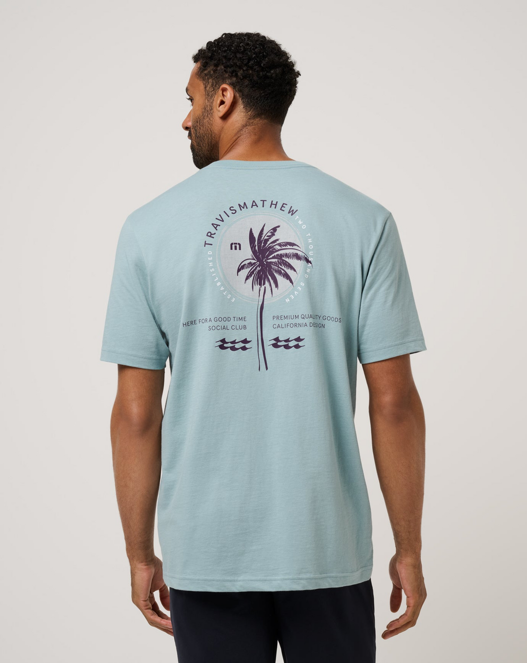 Back view of TravisMathew Hold My Calls Tee in light blue featuring large palm graphic print