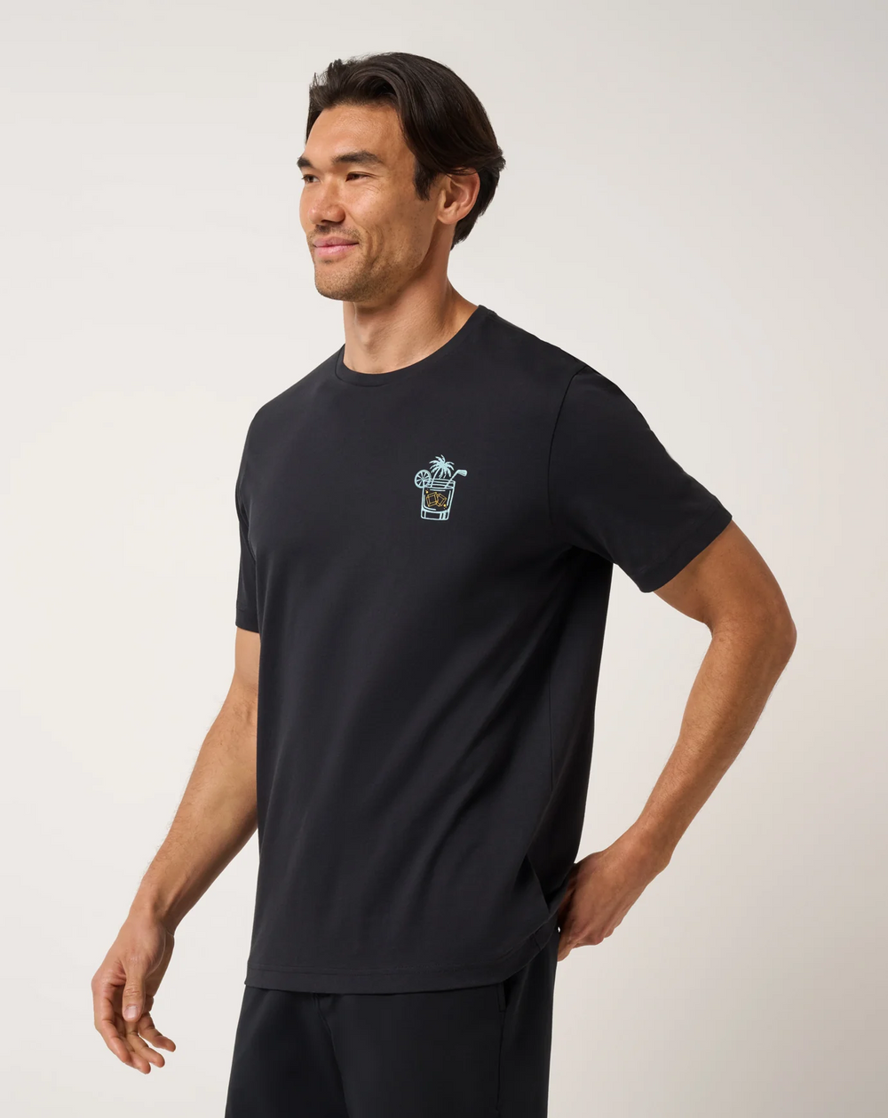 TravisMathew Beverage Cart Tee in black shown from side angle with small chest graphic