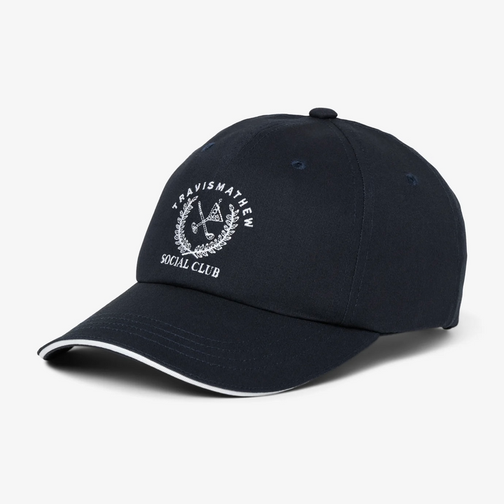 Angled view of TravisMathew Social Club navy cap with curved brim and piping