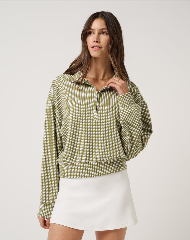 TravisMathew women’s Printed Skyloft Soft Echo half zip pullover in green houndstooth worn with white golf skirt.