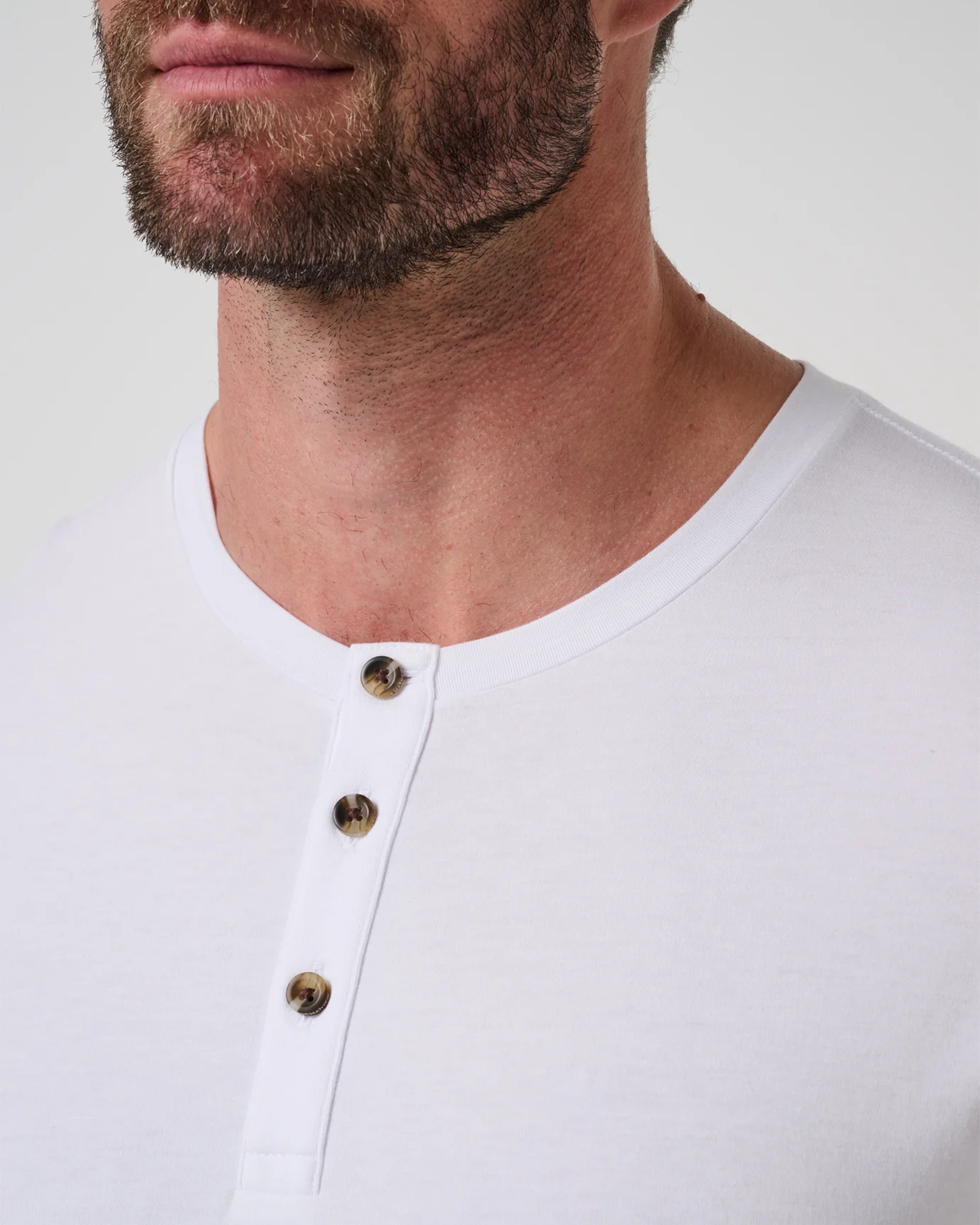 Close-up of the three-button henley placket with tortoiseshell-look buttons and rounded neckline on the TravisMathew Cloud Henley Tee in white