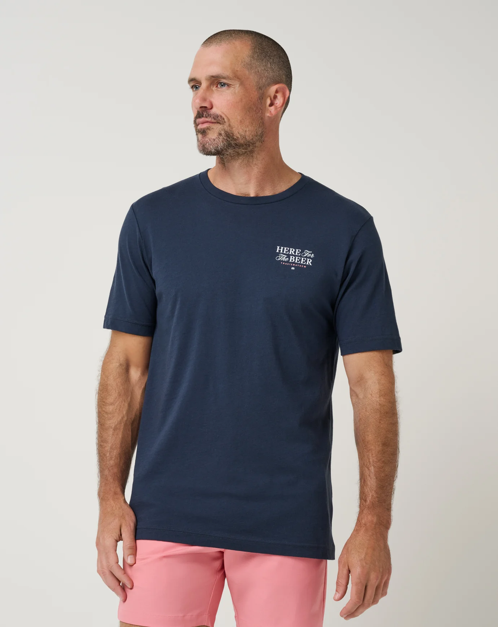 TravisMathew Stout Standard Tee in navy, front view on model showing the classic crewneck and small chest graphic