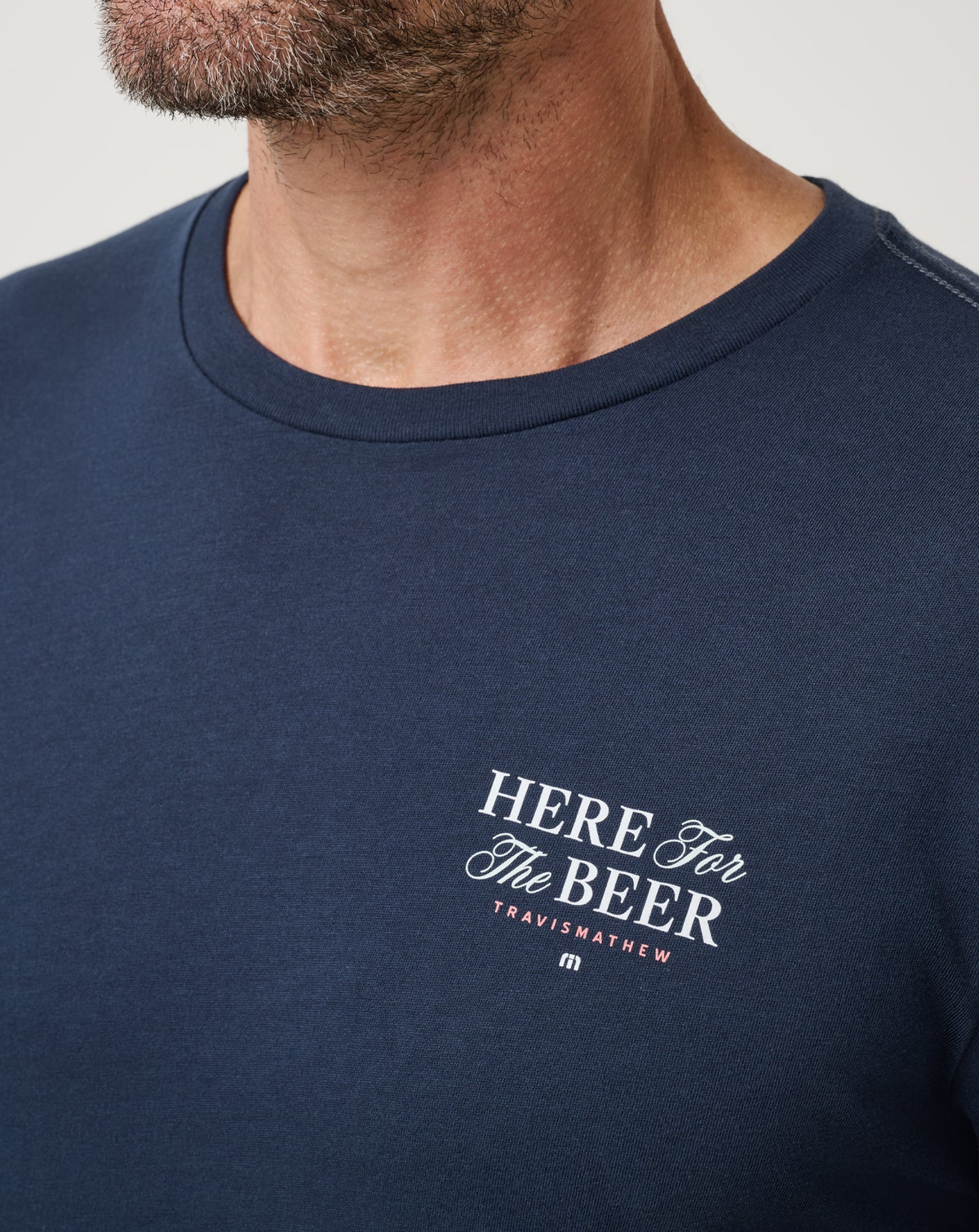 Close-up of the Here For The Beer chest graphic on the TravisMathew Stout Standard Tee in navy