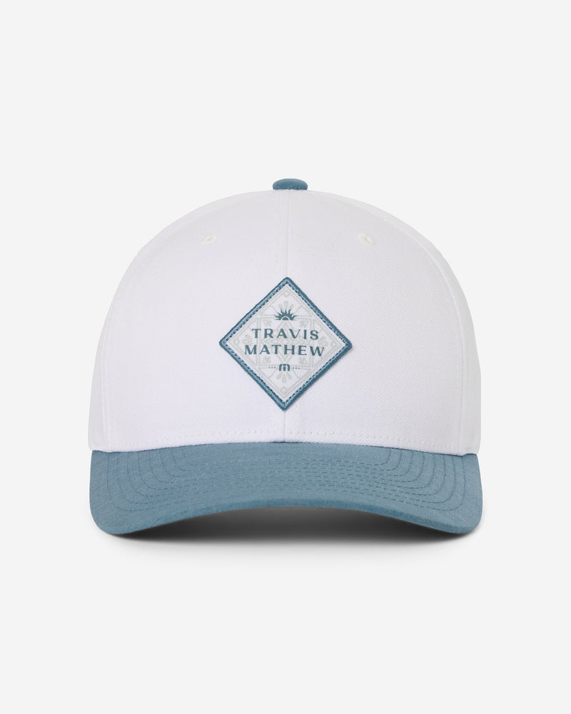 TravisMathew Youth Base Fare Hat in white with contrast blue brim, front view showing the diamond TravisMathew patch
